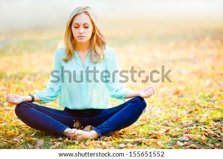 Young beautiful tranquil girl in yoga position with eyes closed on autumn background