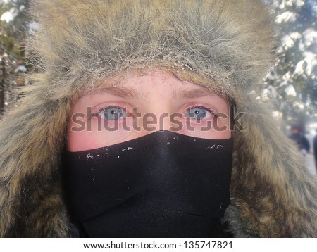 closeup of face of male teenager with furry hat and balaclava, blue eyes with frost ice crystals