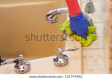closeup of hands with purple latex gloves cleaning  bathroom with green microfiber cloth
