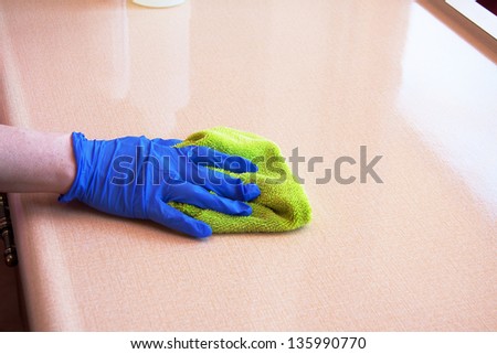 closeup of hand with purple latex glove cleaning  kitchen counter top with green microfiber cloth