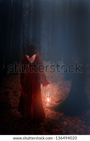 caucasian brunette woman in dark  scary woods with red velvet dress and lamp, walking away in circle of light, dark gloomy forest