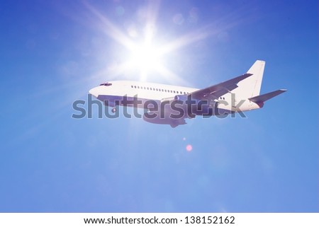 passenger jet in flight against clear blue sky with sun rays and flares landing gear down