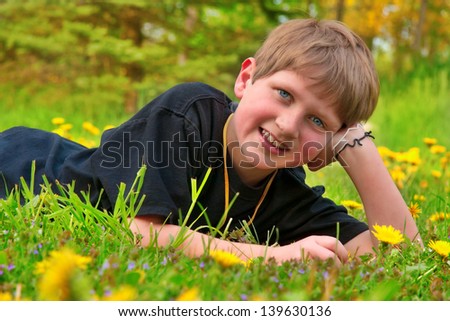 young happy handsome caucasian boy laying down in a field of yellow dandelion flowers