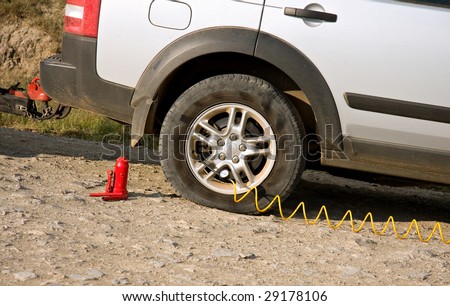 flat tire of dusty dirty car being re-inflated by small compressor pump
