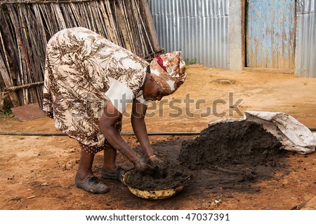 elderly african woman preparing a mixture of cow dung and mud used as a floor covering in traditional huts