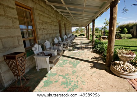 perspective shot of many white wooden chairs on veranda of old stone building in shade to rest and relax