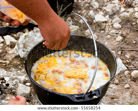 cooking breakfast in black iron pot gas stove while camping hand throwing in cheese