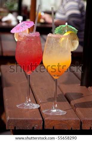 yellow and pink cocktails on wooden table in outdoor cafe with straws and umbrellas