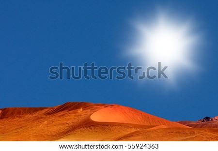 Desert landscape shot with red dunes and blue sky with big white sun and yellow grass in the foreground in Namibia