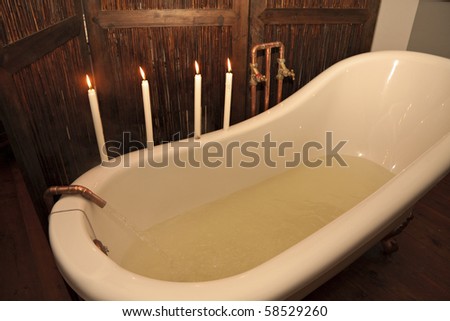water pouring into vintage bath from bronze tap with four candles preparing for romantic bath