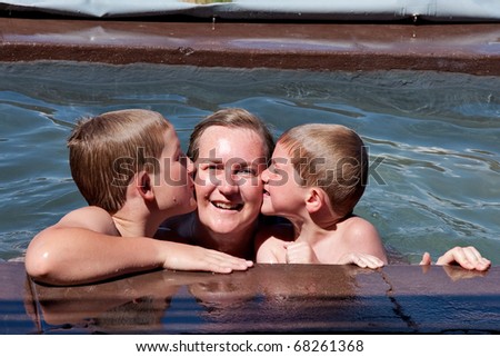 Adorable siblings kissing their mother in swimming pool