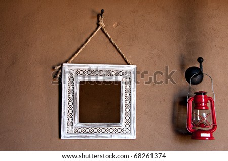 vintage style white frame mirror and red storm lantern on brown mud wall