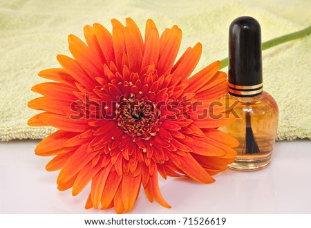 nail care product bottle with orange gerbera daisy flower  on light green towel