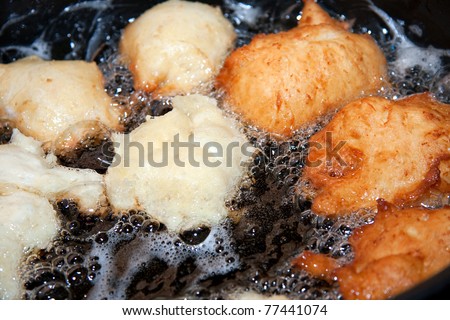 frying balls of doughnut batter in hot oil in cast iron pot on a stove, closeup with oil bubbling, some raw and some golden brown