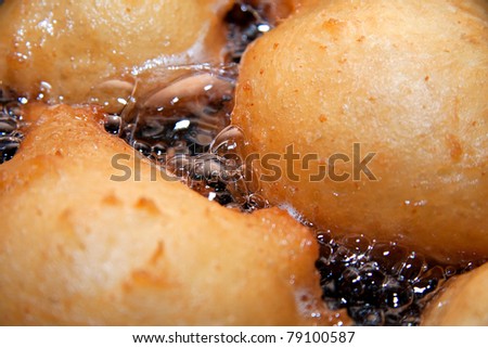 frying balls of doughnut batter in hot oil, closeup with oil bubbling