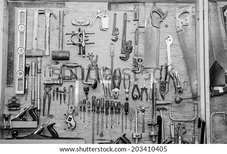 assortment of DIY tools hanging in a wooden cupboard against a wall in a work shed. Black and white image
