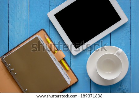 Empty coffee cup with tablet pc and notebook with pen on the office desk