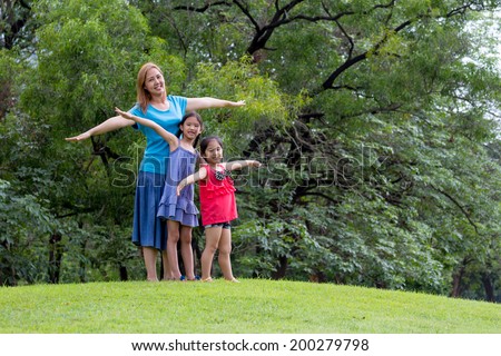 Happy Asian mother and daughter with raised arms in park. Freedom and happiness family concept