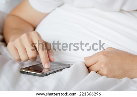 Asian man touching screen of smart phone on the bed