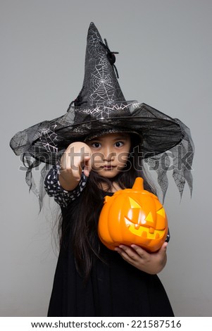 Portrait of little Asian girl in black hat and black clothing with pumpkin