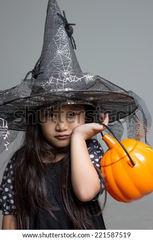 Portrait of little Asian girl in black hat and black clothing with pumpkin