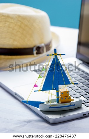 Ship toy on the laptop and sun hat, travel concept.