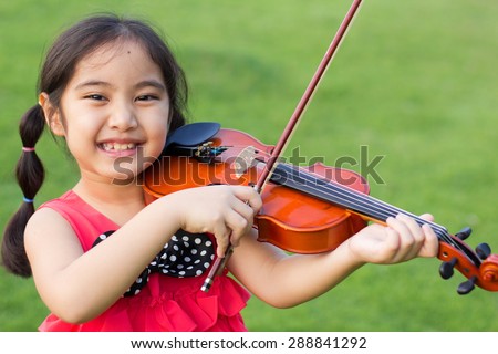 Little Asian child playing violin in the park