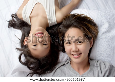 Portrait of happy Asian mother lying  with daughter on the bed