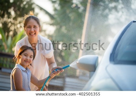 Happy Asian girl washing car with her mother at home