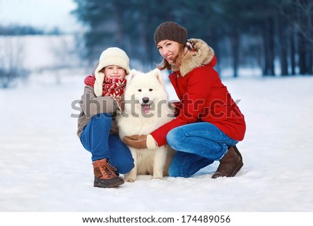 Beautiful happy family, mother and son walking with white Samoyed dog outdoors in winter day