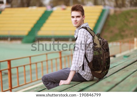 Handsome young smiling man with backpack, modern hipster in urban style looking on camera