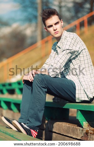 Free hipster man sitting on a bench in the city, sunny summer evening, looks away