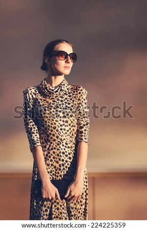 Street fashion portrait stylish pretty woman in a dress with leopard print and sunglasses posing in city on evening sunny sunset