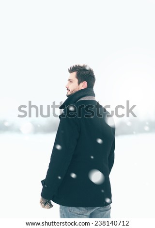 Handsome man outdoors standing in the winter blizzard looks into the distance