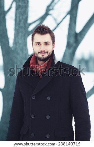 Handsome bearded man with stylish hairstyle in black coat outdoors in winter day