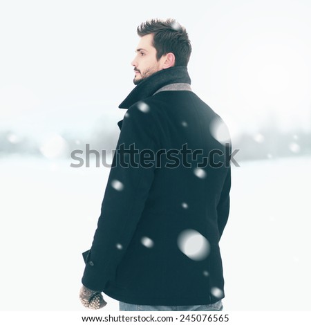 Handsome elegant man standing outdoors in the winter blizzard and looks into the distance