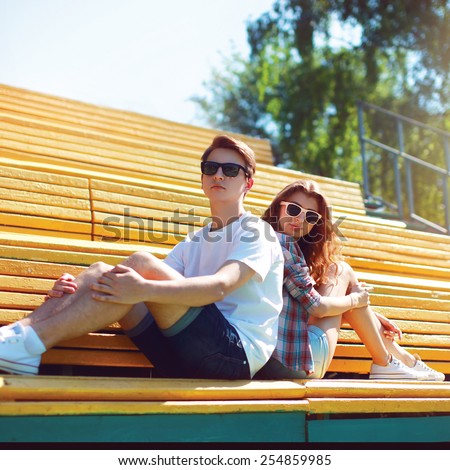 Fashion hipster couple in sunglasses sitting on the bench city park in sunny summer day