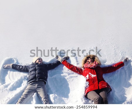 Mother and son having fun together lounging in the snow on a sunny winter day, copy space