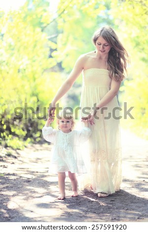 Sunny photo mother and child walking barefoot in the forest, mom helps the baby to take the first steps on a summer day