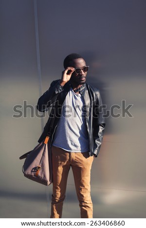 Handsome african man in leather jacket and sunglasses against the metal urban wall