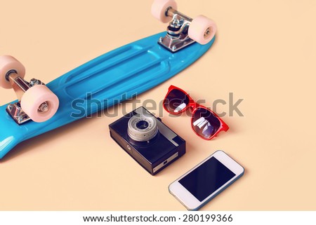 Fashion look concept. Blue skateboard, red sunglasses, vintage camera and screen smartphone. Trendy colorful photo