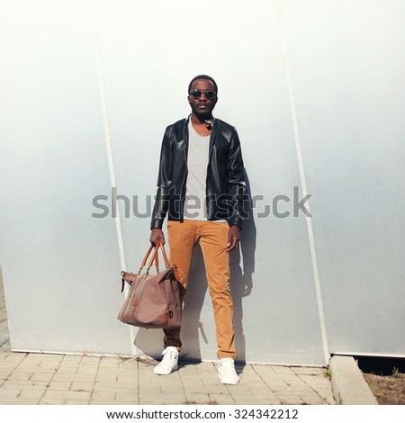 Fashion handsome african man model wearing a sunglasses and black leather jacket with bag in city