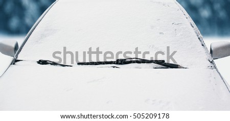 Frozen car covered snow in winter day, view front window windshield and hood on snowy background