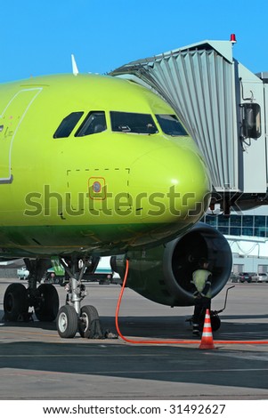 Green airplane loads fuel at the hub of international airport