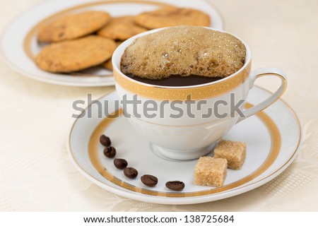 Cup of coffee with more cream, coffee beans, two brown sugar cubes and biscuits on background