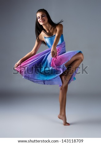 Beautiful female modern jazz contemporary style dancer on a grey background. Dancer is barefoot and wearing a blue and purple dress.