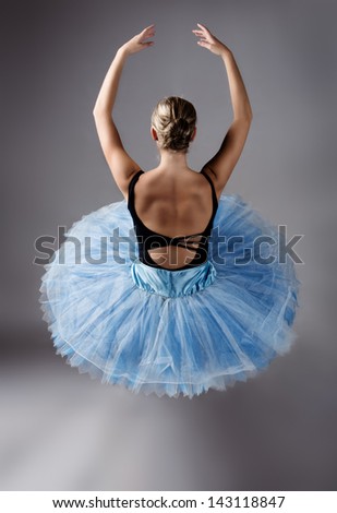 Beautiful female ballet dancer on a grey background. Ballerina is wearing a black leotard; pink stockings; pointe shoes and a blue tutu.