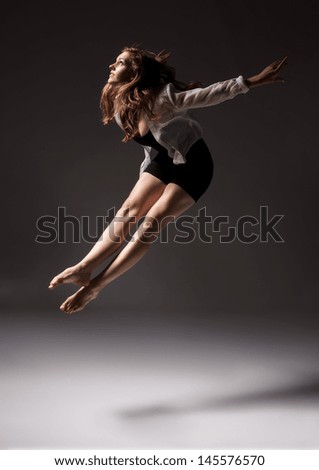 Beautiful slim young female modern jazz contemporary style ballet dancer wearing a black leotard and white shirt on a neutral grey studio background