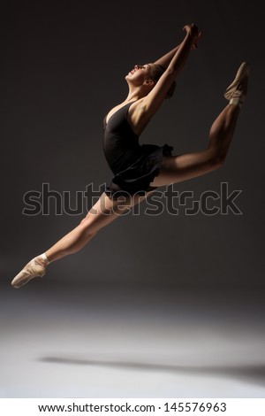 Beautiful young female classical ballet dancer on pointe shoes wearing a black leotard and skirt on a neutral grey studio background