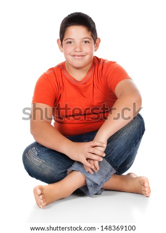 Young caucasian boy wearing an orange t-shirt and blue jeans. The boy is sitting and smiling.
